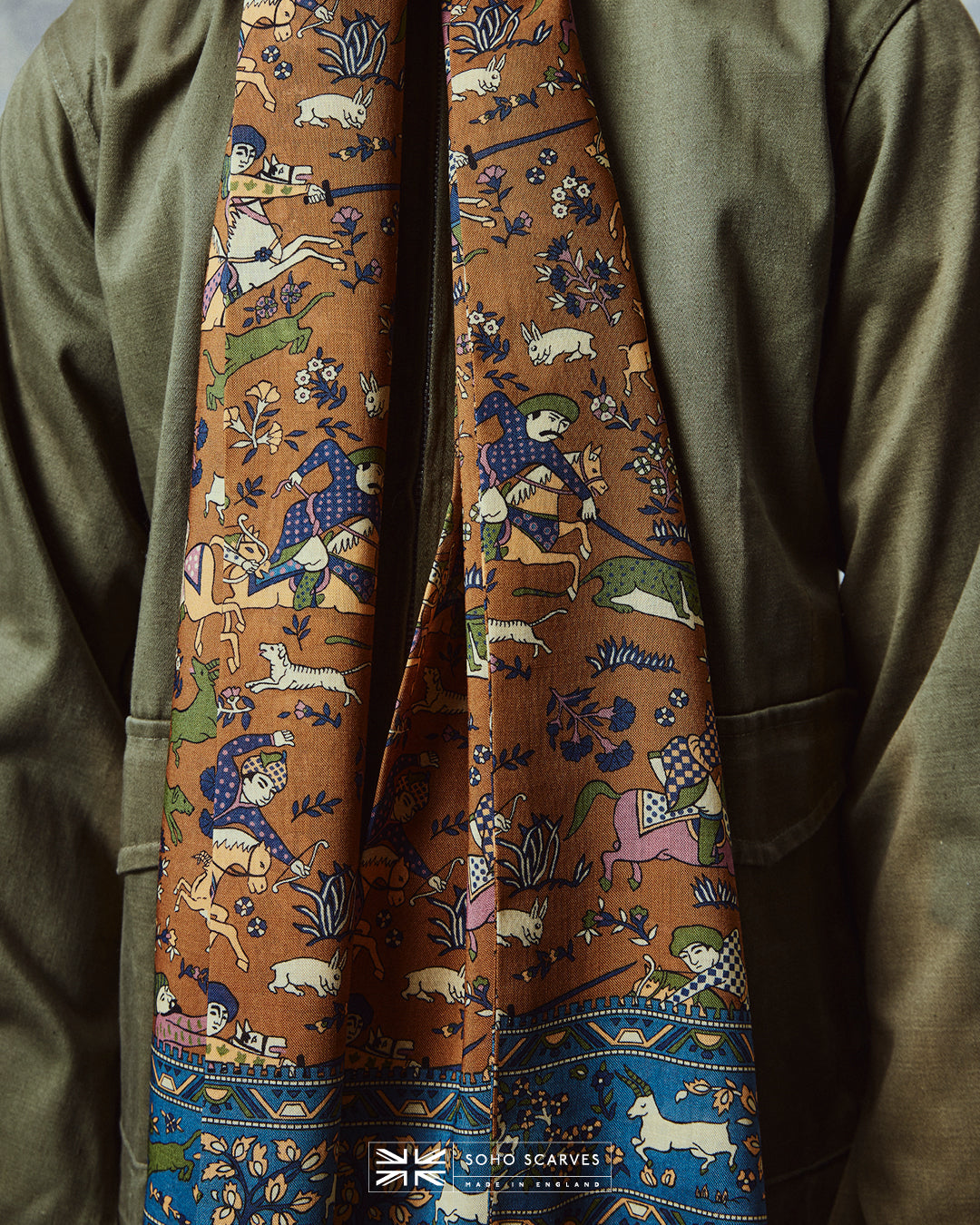 Close-up wearing the English-made, 'Hunters in Dull Gold' silk and wool scarf, with focus on the multicoloured design on a dull gold ground, combining ancient East Asian hunting motifs.