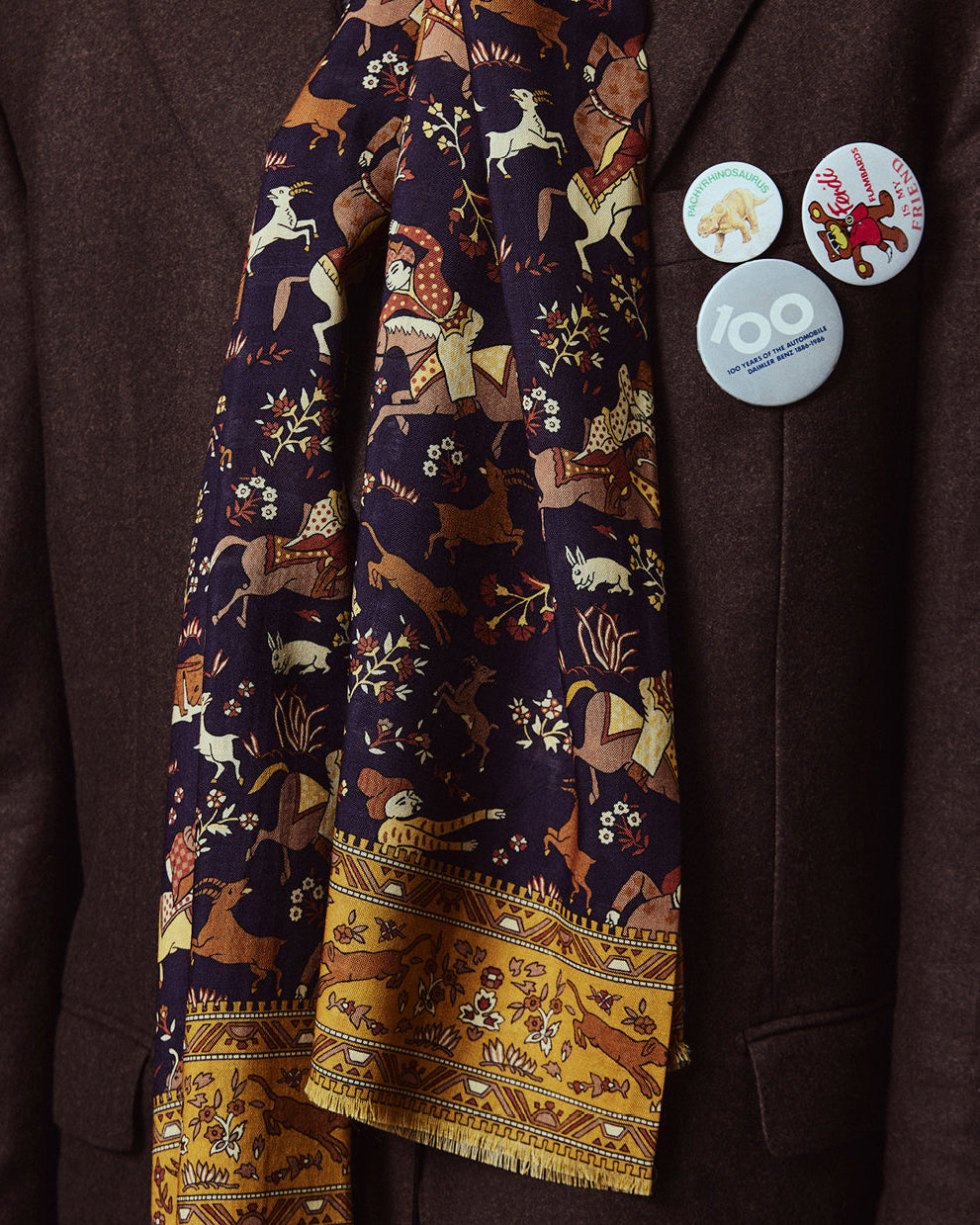 Close-up wearing the English-made, 'Hunters in Indigo' silk and wool scarf, with focus on the blue, brown, and yellow design, combining ancient East Asian hunting motifs.