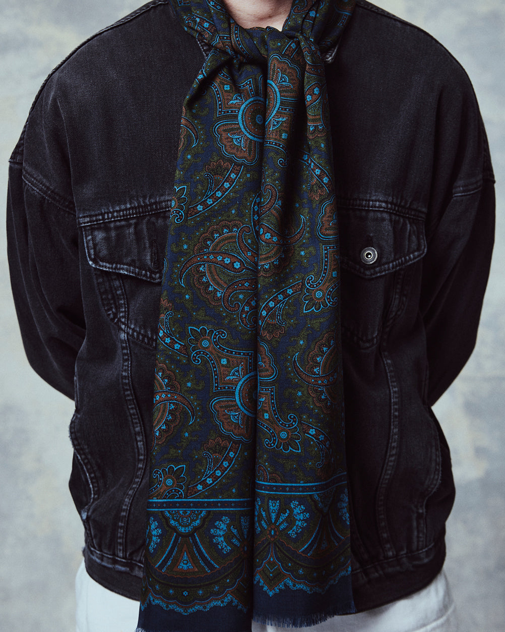 Close-up of man wearing the English-made, 'Paisley in Navy' silk and wool scarf, with focus on the blue, orange and green paisley design.