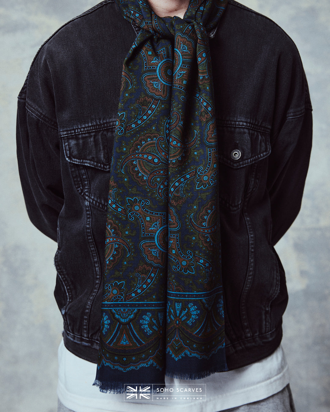 Close-up of man wearing the English-made, 'Paisley in Navy' silk and wool scarf, with focus on the blue, orange and green paisley design.