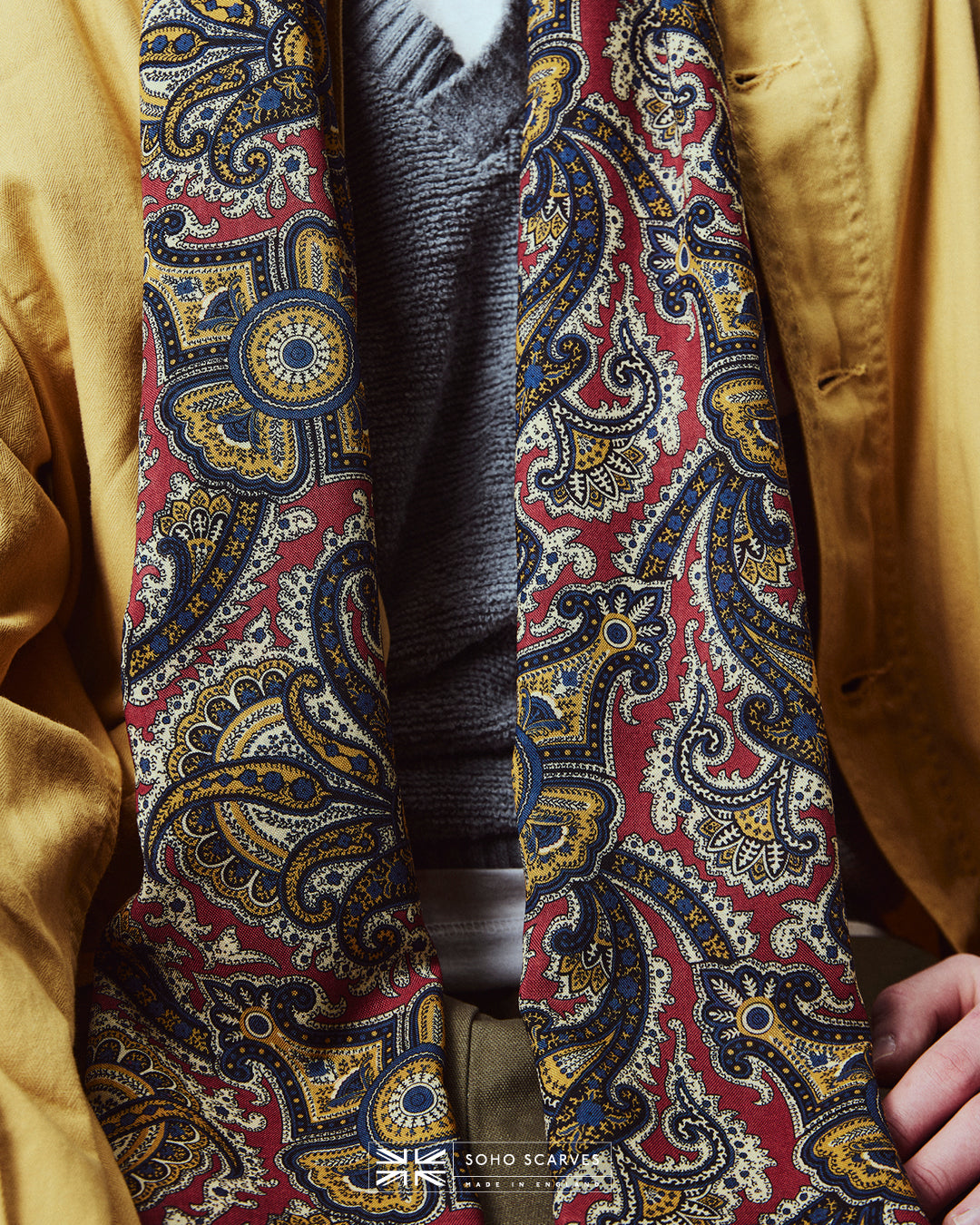 Close-up of man wearing the English-made, 'Paisley in Red' silk and wool scarf, with focus on the red, blue and yellow paisley design.