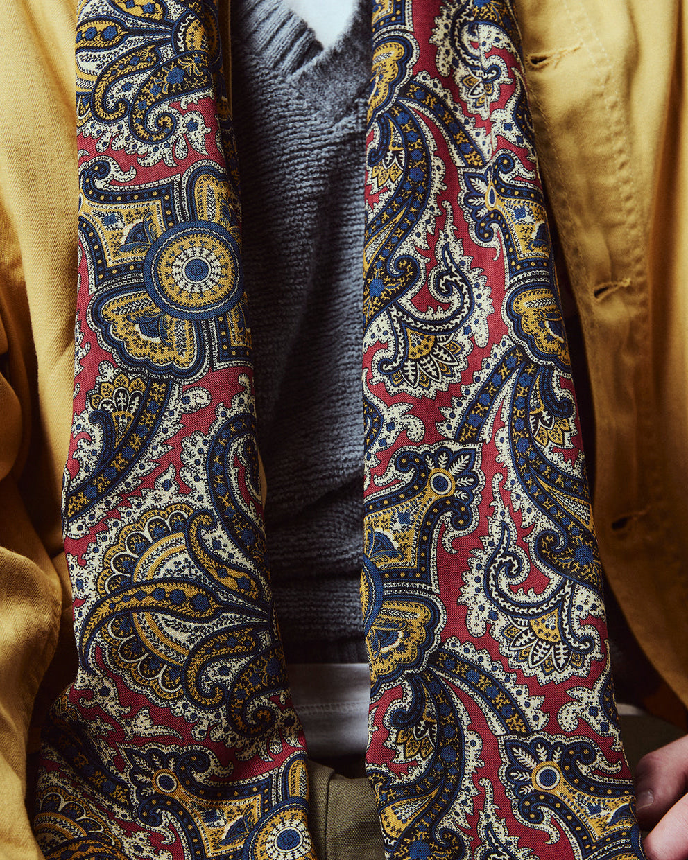 Close-up of man wearing the English-made, 'Paisley in Red' silk and wool scarf, with focus on the red, blue and yellow paisley design.