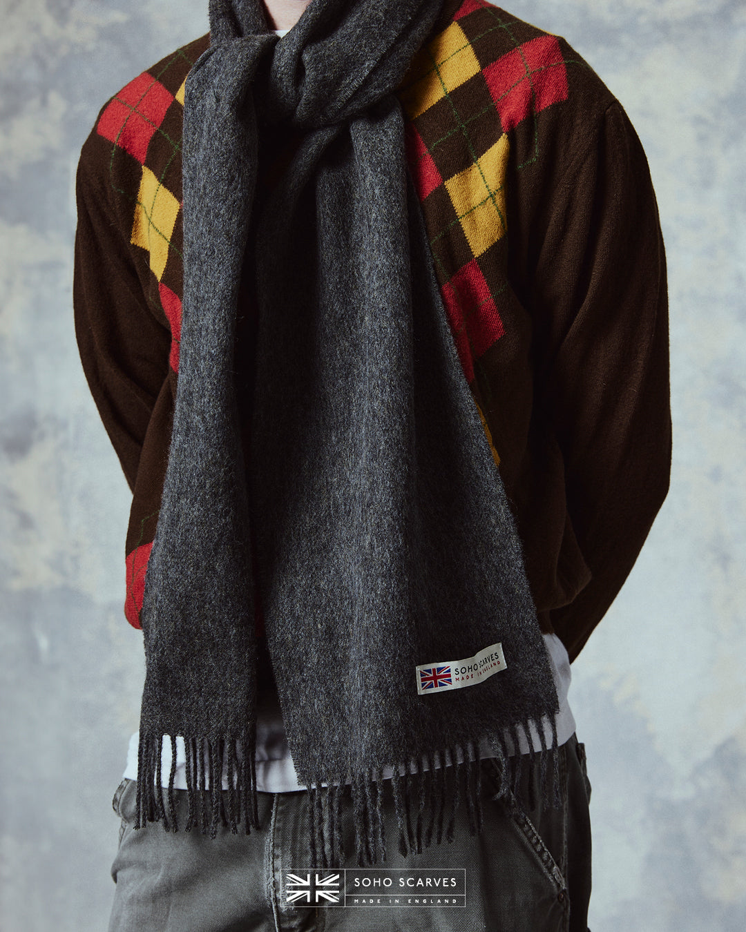 Close up of man wearing the Yorkshire-made, 'Lowlands in Grey' wool scarf, with focus on the 'Soho scarves, Made in England' label and matching fringes.