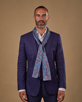 Portrait view of male model wearing 'The Dean' silk scarf. Tied loosely around neck in a simple knot and shoulders and paired with a smart, midnight-blue suit.
