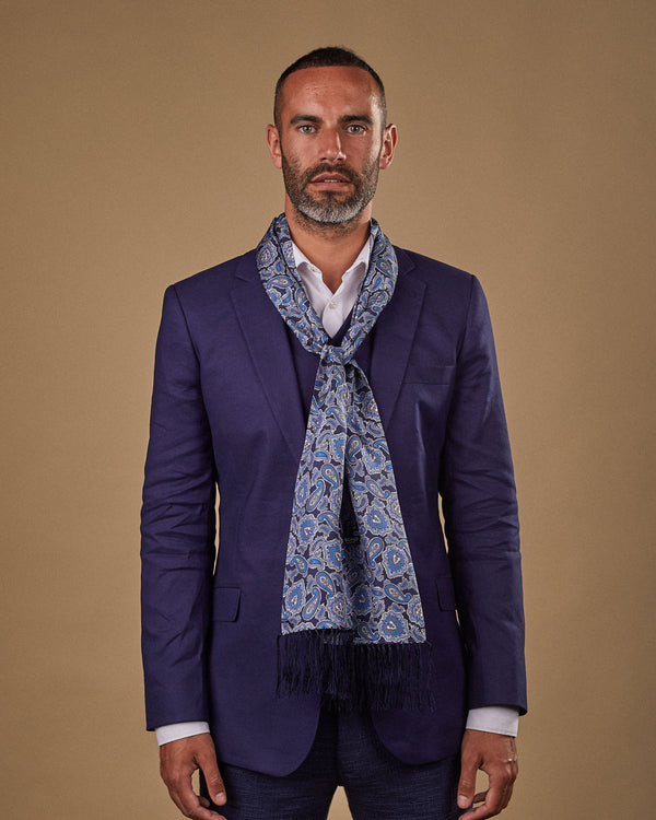 Portrait view of male model wearing 'The DeZon' silk aviator scarf. Tied loosely around neck in a simple knot and shoulders and paired with a smart, midnight-blue suit.