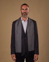 Portrait view of male model looking straight ahead, wearing 'The Grant' silk aviator scarf. Draped loosely around shoulders and neck and paired with a smart, dark suit.