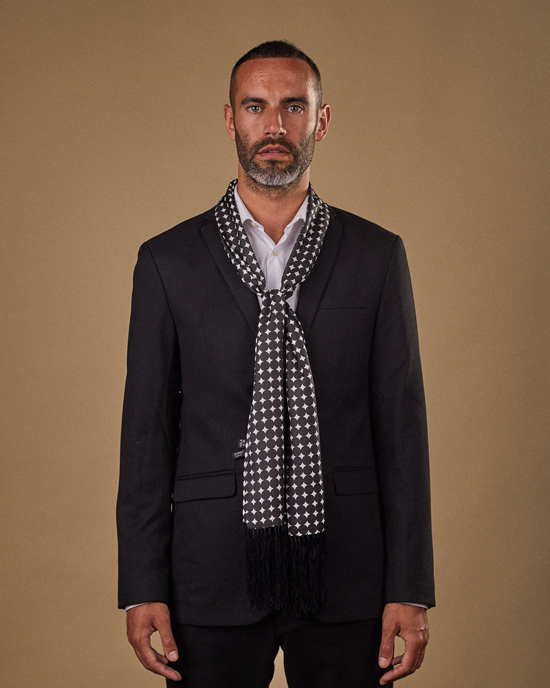 Portrait view of male model wearing 'The Grant' silk aviator scarf. Tied loosely around neck in a simple knot and shoulders and paired with a smart, dark suit.