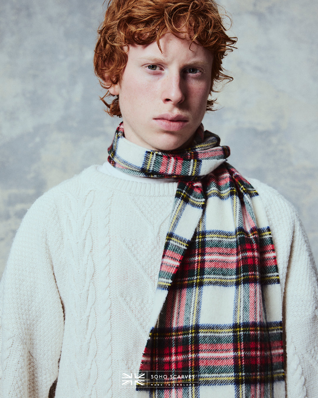 Top-half view of man wearing the Yorkshire-made, 'Highlands Tartan Dress' scarf in red, blue, green and yellow against a pale cream ground.