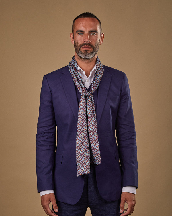 Portrait view of male model wearing 'The Koenji' polyester scarf. Tied loosely around neck in a simple knot and shoulders and paired with a smart, midnight-blue suit.