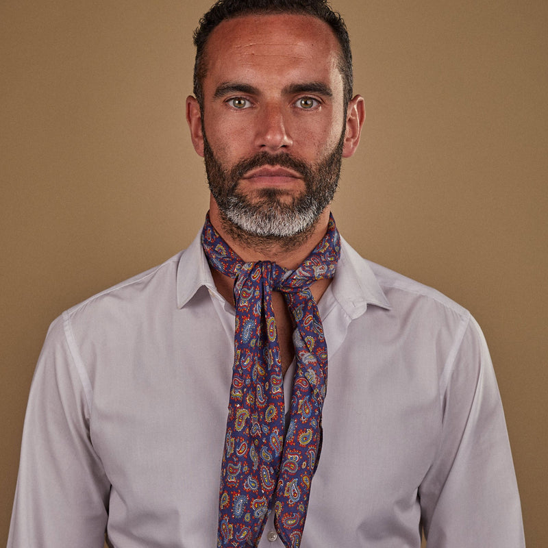 Man wearing 'The Lexington' multicoloured paisley bandana. Tied snugly around neck in a simple knot and paired with a white shirt.