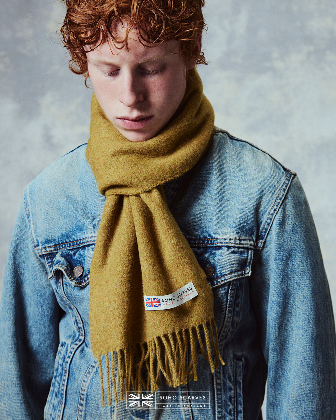 Close up of man wearing the Yorkshire-made, 'Lowlands in Gold' wool scarf, with focus on the 'Soho scarves, Made in England' label and matching fringes.