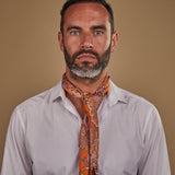 Man wearing 'The Niagra' orange and pink floral bandana. Tied snugly around neck in a simple knot and paired with a white shirt.