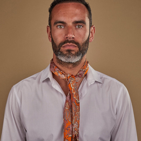 Man wearing 'The Niagra' orange and pink floral bandana. Tied snugly around neck in a simple knot and paired with a white shirt.