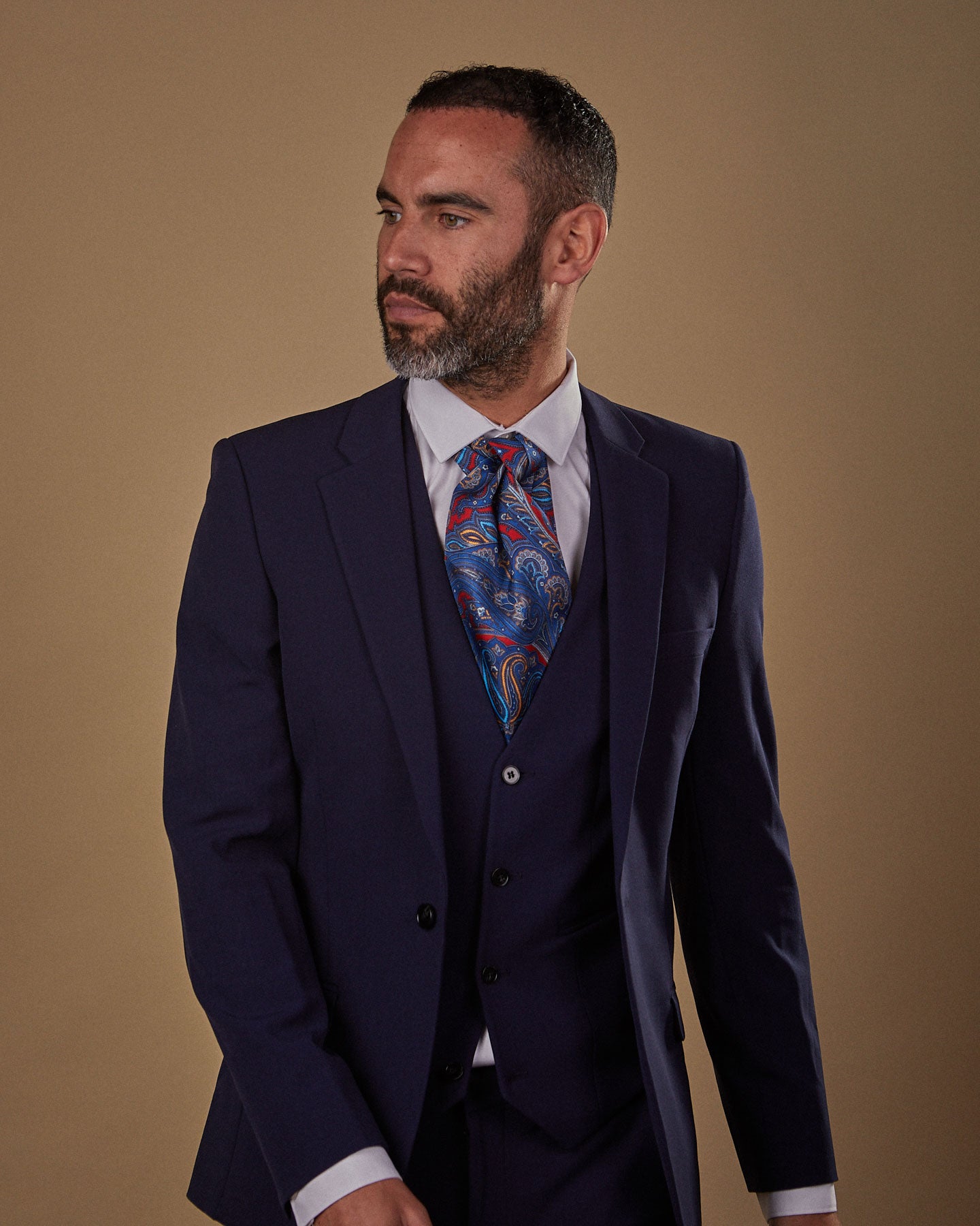 Walking pose, wearing an Oxford silk Double Ascot tie from SOHO Scarves, paired with white shirt and three-piece midnight blue suit.