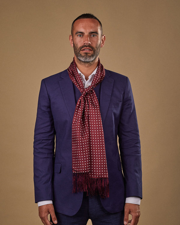 Portrait view of male model wearing 'The Sapporo' silk aviator scarf. Tied loosely around neck in a simple knot and shoulders and paired with a smart, midnight-blue suit.