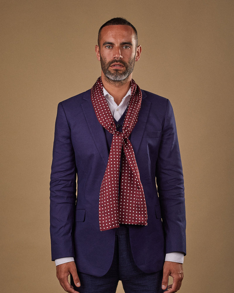 Portrait view of male model wearing 'The Sapporo' silk scarf. Tied loosely around neck in a simple knot and shoulders and paired with a smart, midnight-blue suit.