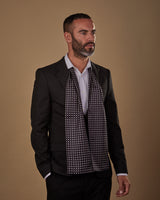 Three quarters front view of model facing slightly to his left, wearing 'The Shinagawa' polka dot polyester scarf hanging loosely round neck. Paired with white shirt and charcoal suit with hand in pocket.