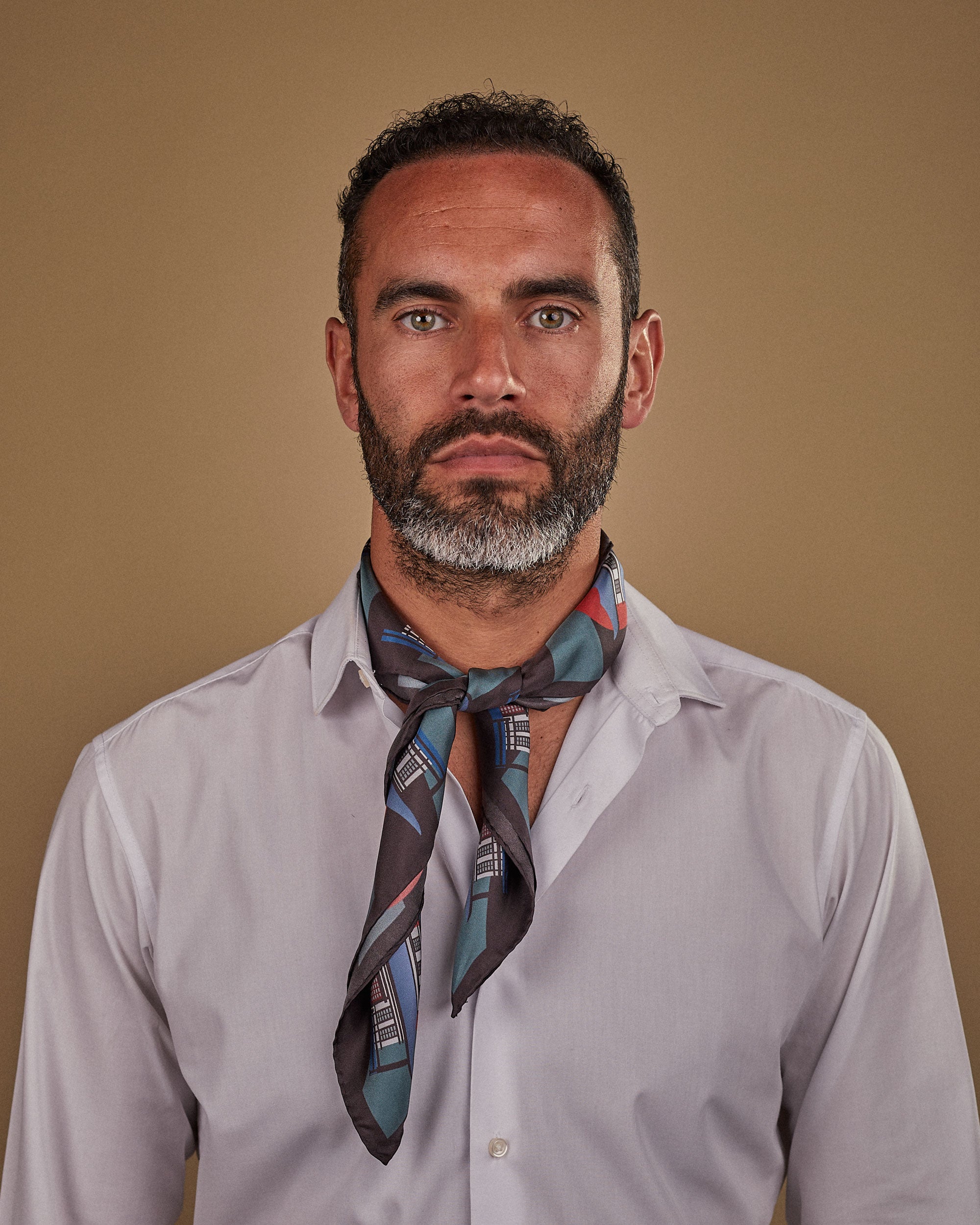 Head and shoulders view of model wearing "The House" Japanese inspired silk neckerchief with knot tie at the front. Paired with white shirt.