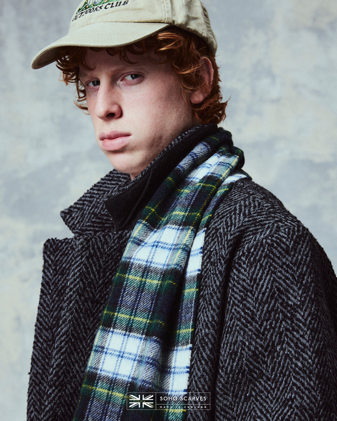 Top-half view of man wearing the Yorkshire-made, 'Highlands Tartan in Green' wool scarf from Soho Scarves, showing the yellow, blue, cream and green tartan pattern.