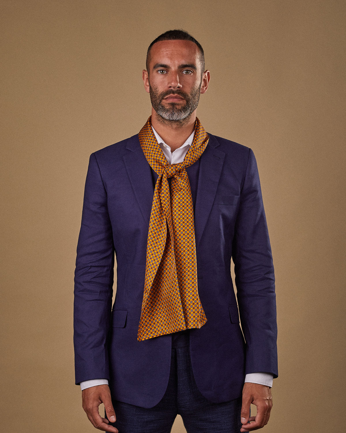 Portrait view of male model wearing 'The Toshima' silk scarf. Tied loosely around neck in a simple knot and shoulders and paired with a smart, midnight-blue suit.