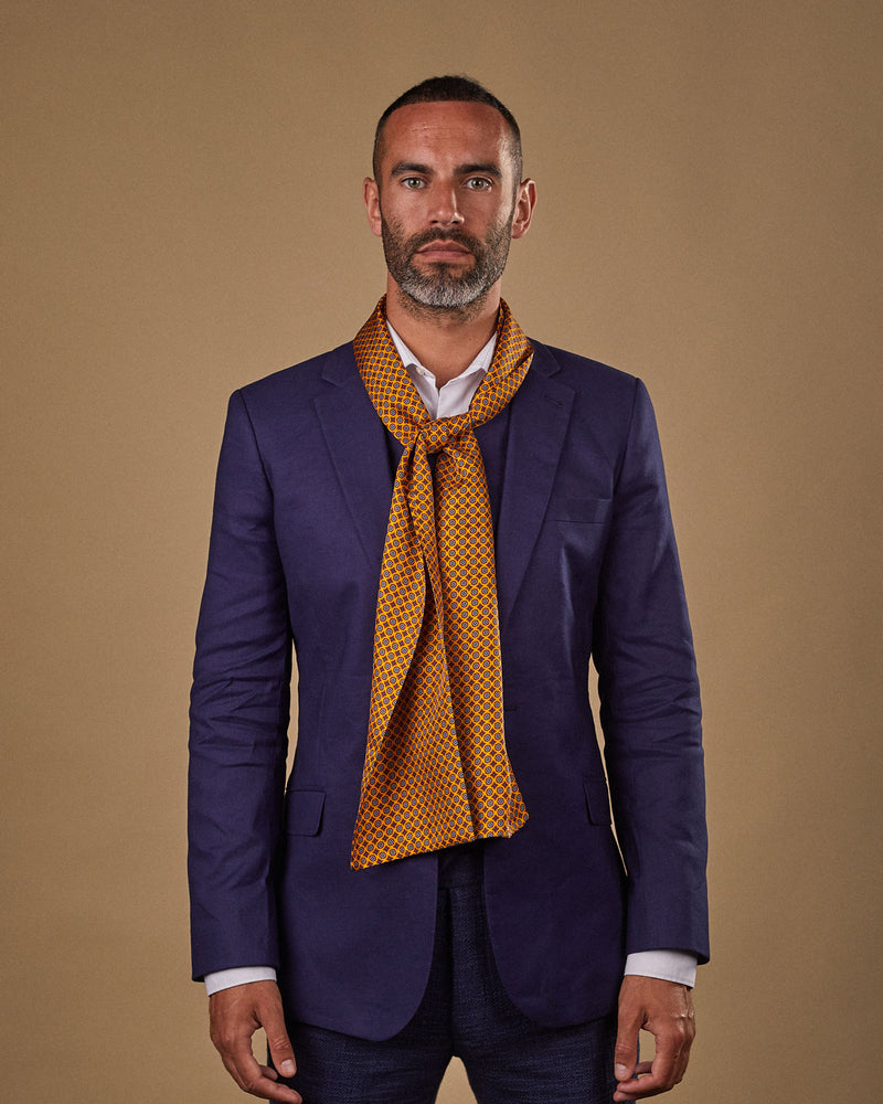 Portrait view of male model wearing 'The Toshima' silk scarf. Tied loosely around neck in a simple knot and shoulders and paired with a smart, midnight-blue suit.