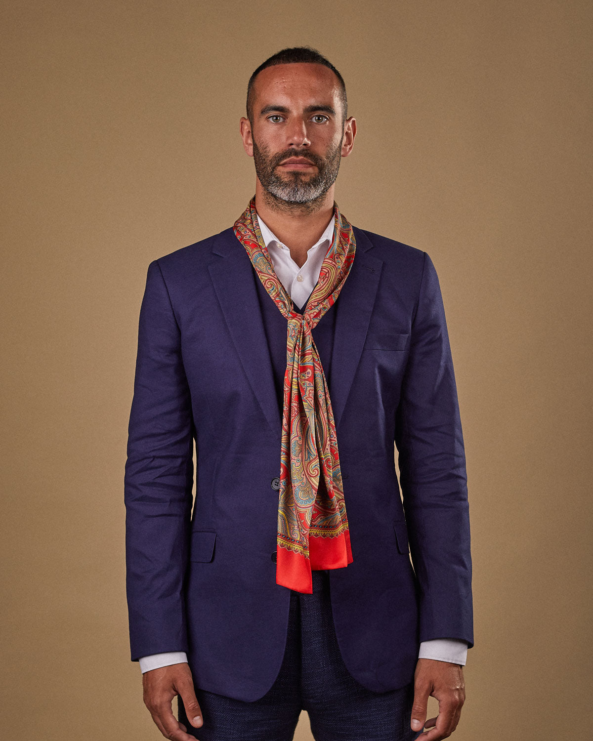 Portrait view of male model wearing 'The Victoria' silk scarf. Tied loosely around neck in a simple knot and shoulders and paired with a smart, midnight-blue suit.