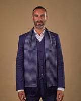 Portrait view of male model looking straight ahead, wearing 'The Westminster' silk aviator scarf. Draped loosely around shoulders and neck and paired with a smart, midnight-blue suit.