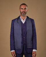 Portrait view of male model looking straight ahead, wearing 'The Westminster' polyester scarf. Draped loosely around shoulders and neck and paired with a smart, midnight-blue suit.