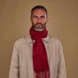 Man wearing Soho Scarves' wine-red cashmere scarf in a classic knot. Paired with fawn three-quarter length coat.