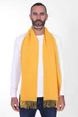 Portrait view of male model looking straight ahead, wearing soft yellow cashmere scarf with fringing. Draped loosely around shoulders and neck and paired with blue jeans and white sweater.