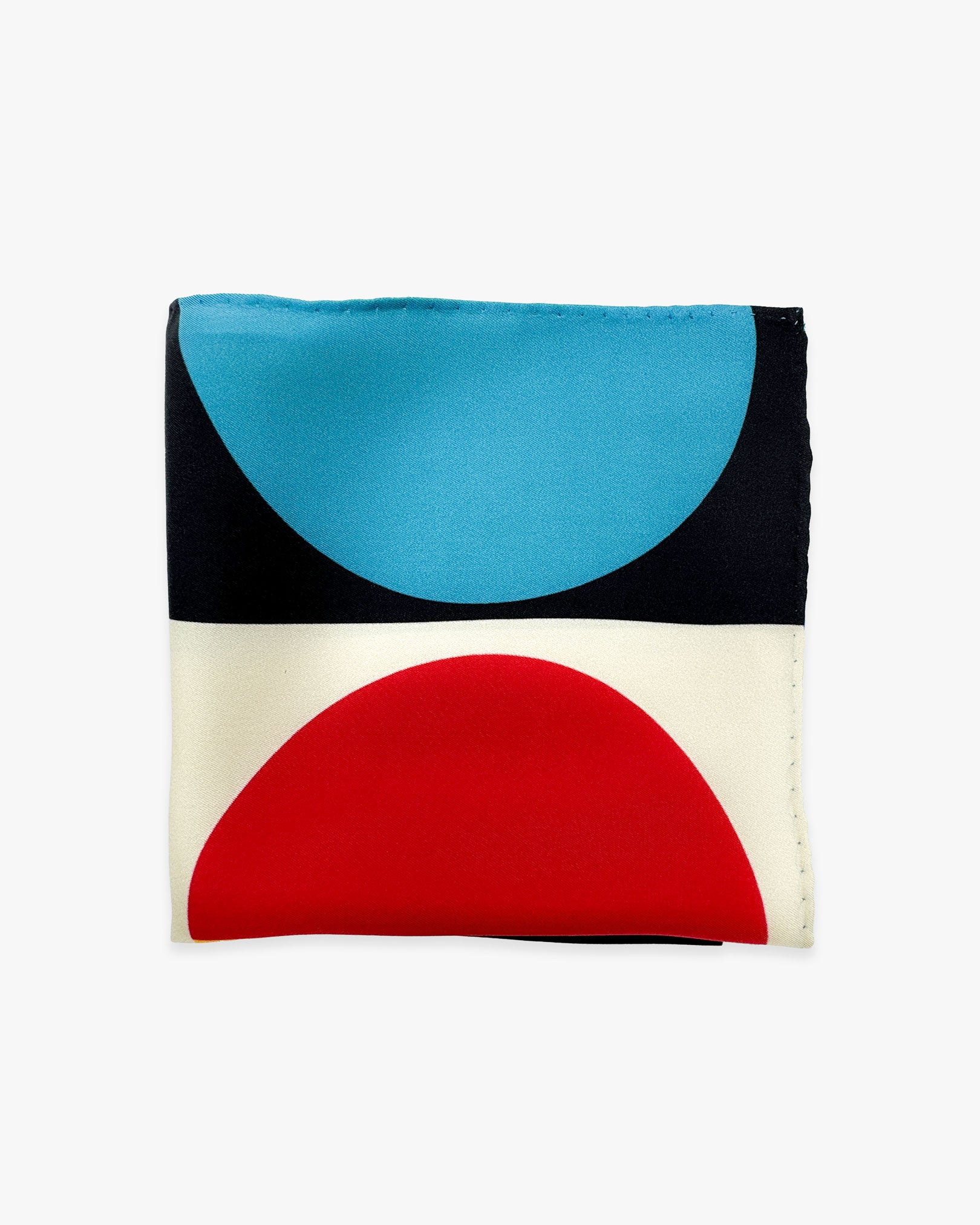 The 'Weimar' silk pocket square from SOHO Scarves folded into a quarter, showing the blue, red and monochrome portion of the semicircular disc pattern.