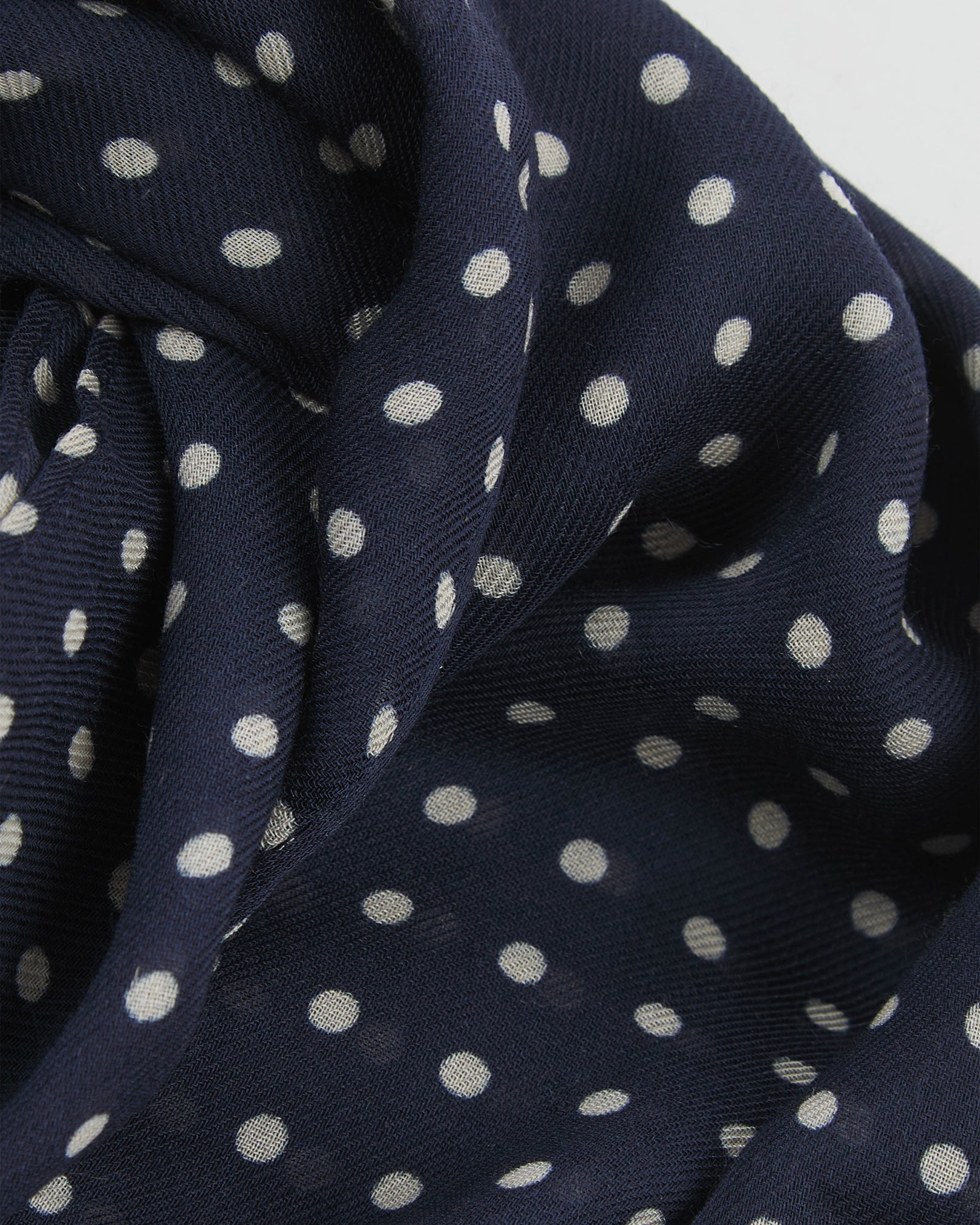 A ruffled close-up of The Westminster bohemian wide scarf, showing the soft modal and wool blend fabric with evenly spaced white polka dots on a navy blue background.