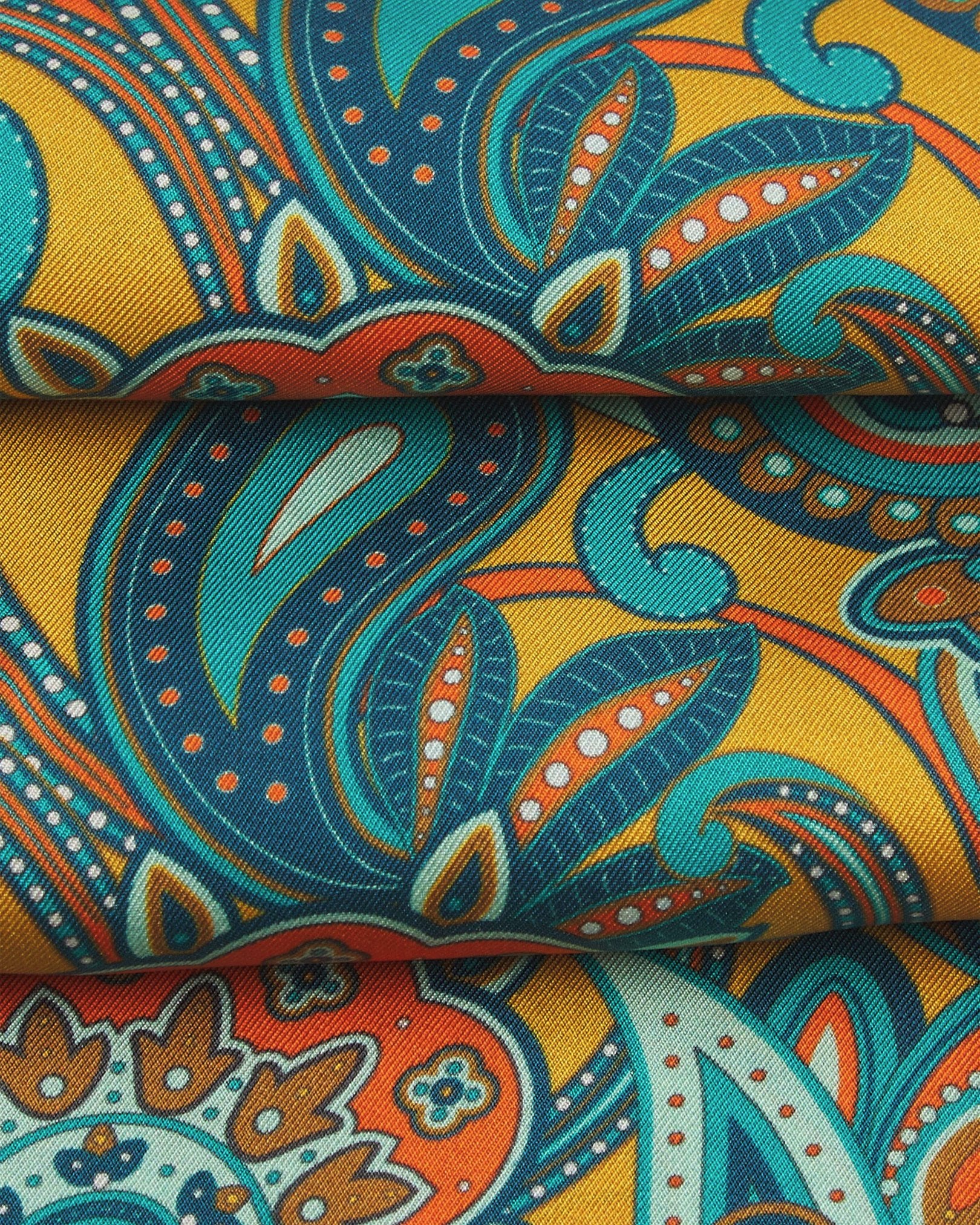 A ruffled close-up of the 'Windermere' gold silk aviator scarf, presenting the overlapping elements of blue, blue-green, orange, and yellow paisley patterns.