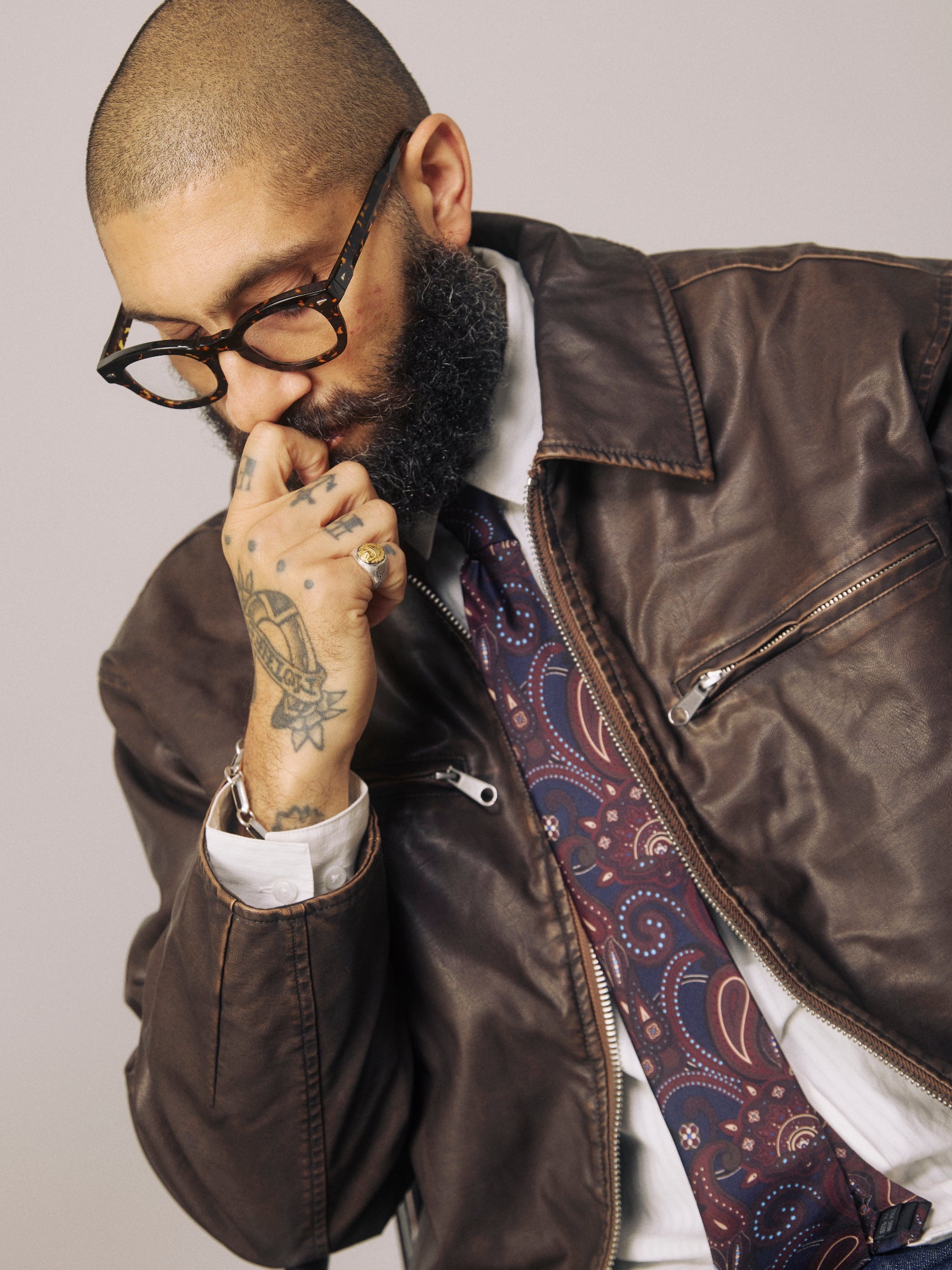 Top-half view of man wearing the 'Windermere Mahogany Haze' paisley silk neck tie in navy and brown. Paired with brown leather jacket.