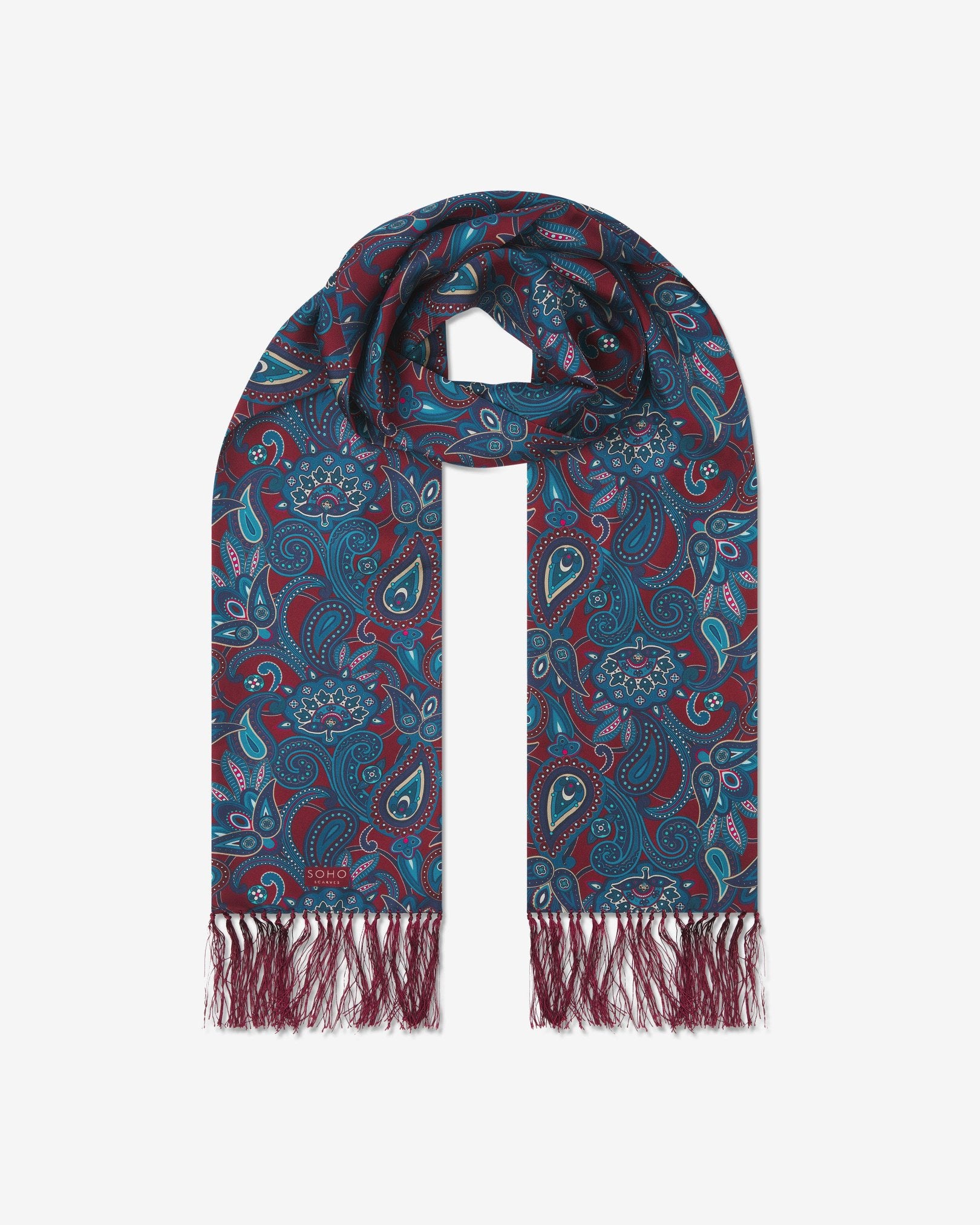 The 'Windermere' rust silk aviator scarf looped with both ends parallel to effectively display the full repeat pattern of blue and blue-green paisley patterns on an rust background with matching fringes.