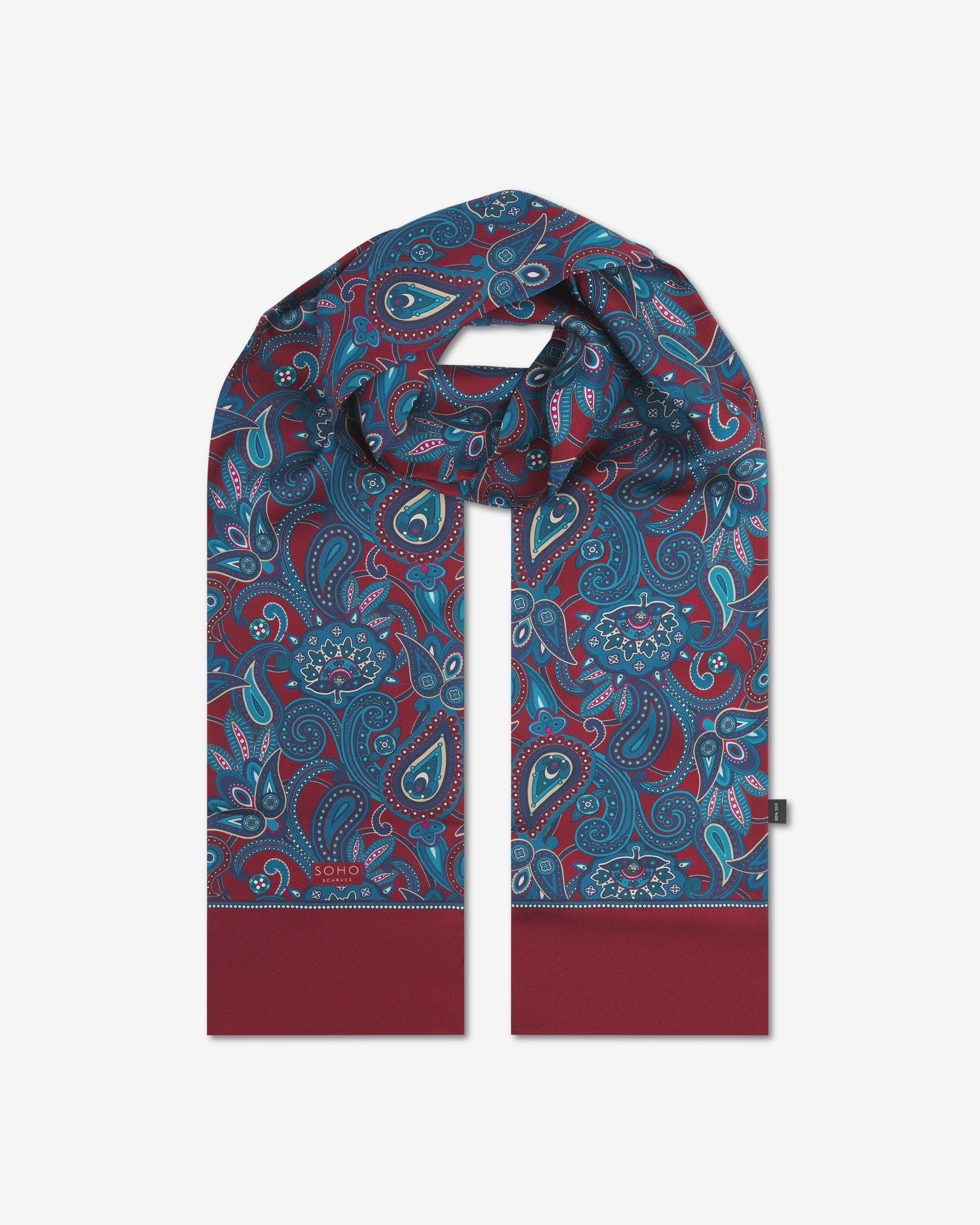 The 'Windermere' rust silk scarf looped with both ends parallel to effectively display the full repeat pattern of blue and blue-green paisley patterns on an rust background