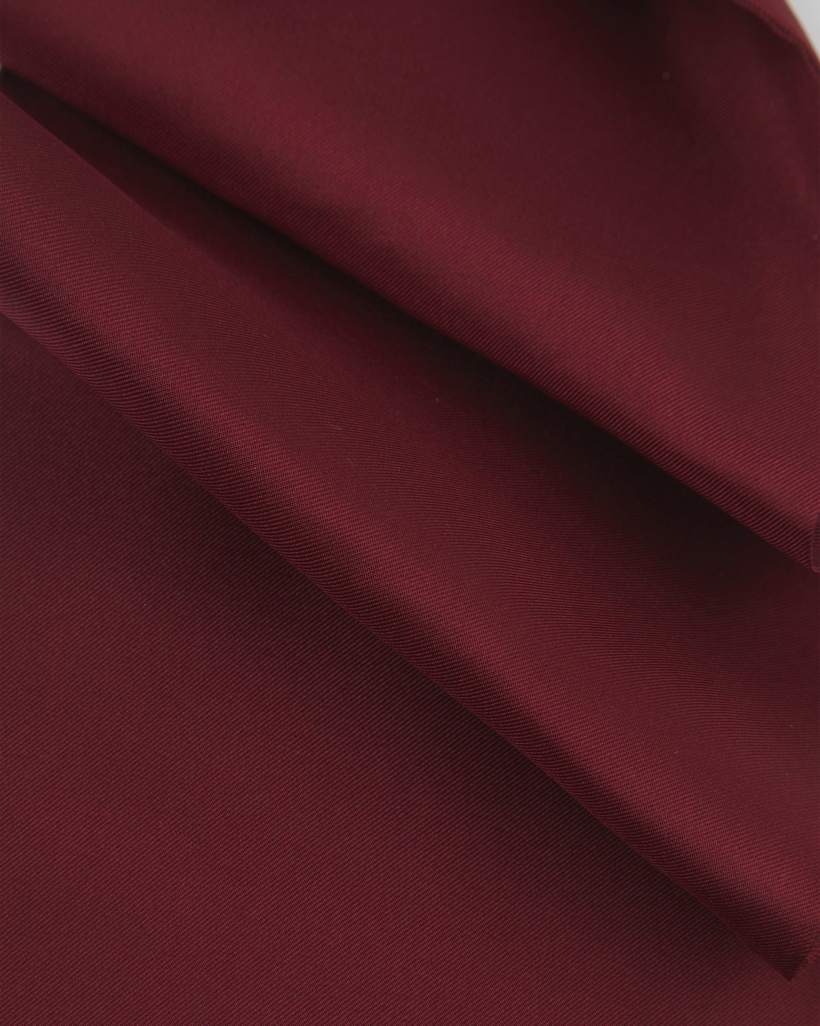 A ruffled close-up of the wine-red silk aviator scarf, presenting the sheen of the fine silk material.