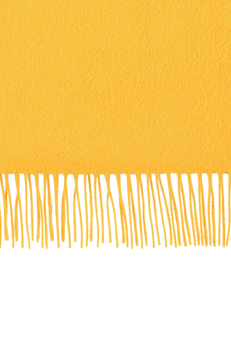 Perfectly horizontal view of the fringe of a yellow pure cashmere scarf from Soho Scarves against a white background.