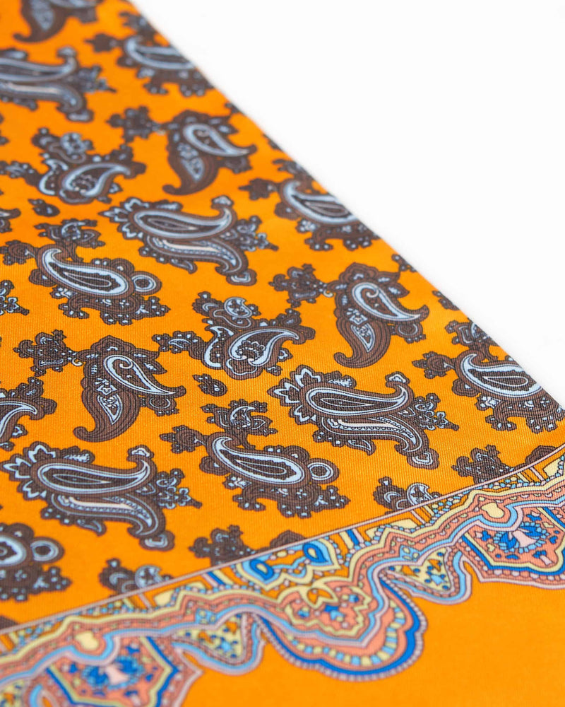 Angled view of the patterned scarf, focussing on the contrasting multi-coloured border and brown paisley patterns.