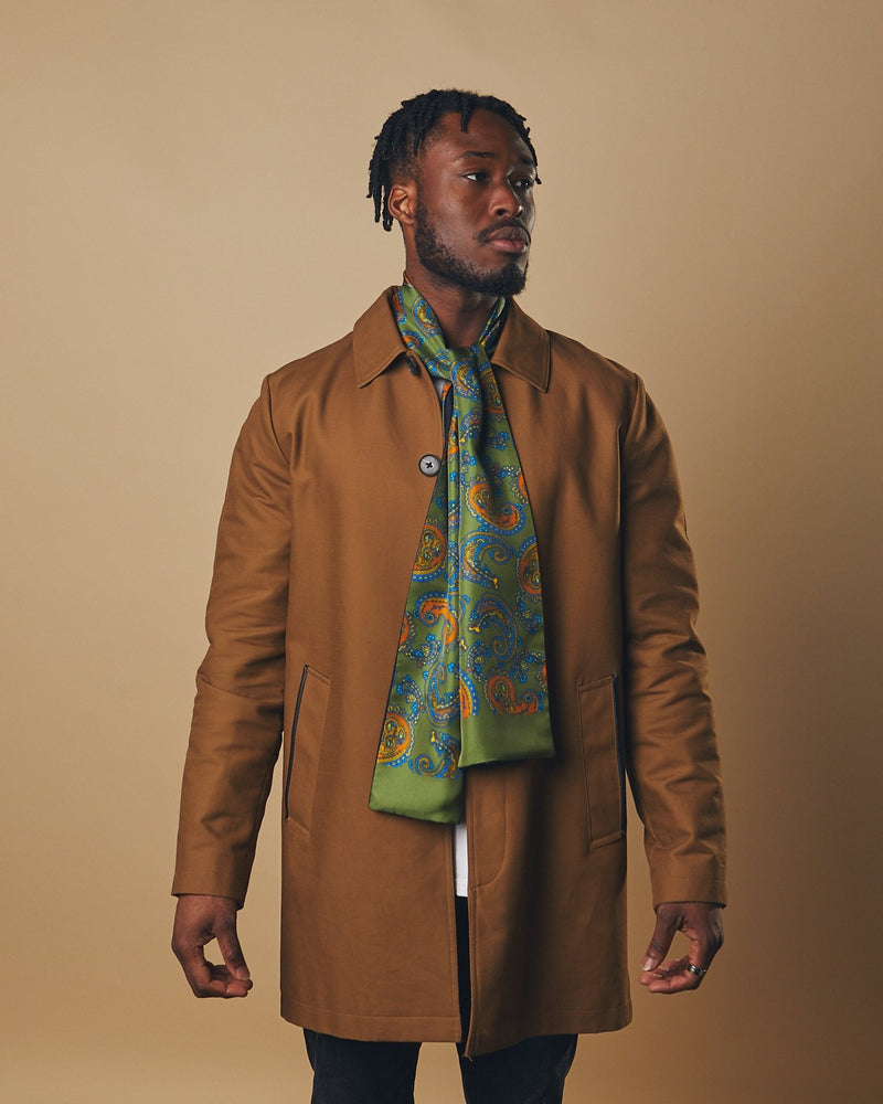 Model looking to his left wearing 'The Carlisle' wool backed silk scarf with clear view of orange paisley patterns. Paired with brown three-quarter length coat. 