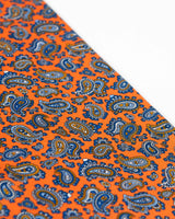Angled view of the light and dark blue paisley patterns on the bright orange scarf.