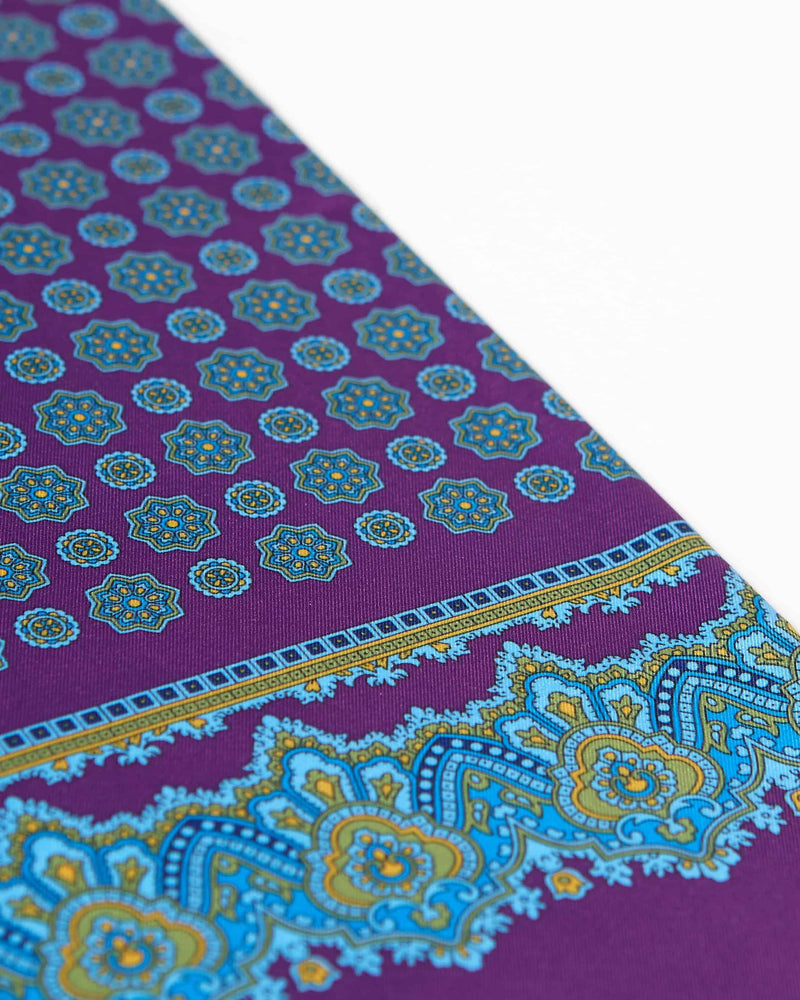 Angled view of the purple and blue geometric patterns with yellow-gold accents on the scarf, with a focus on the elegant border pattern.