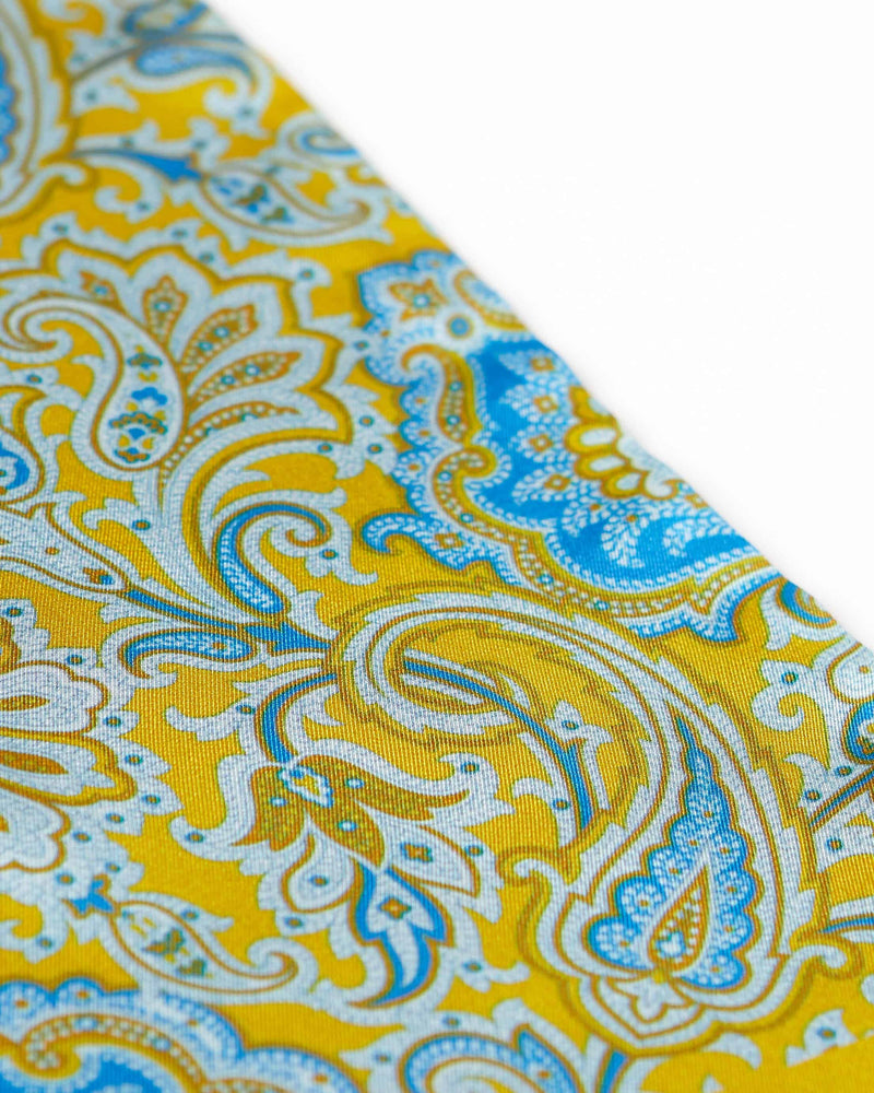 Angled closer view of the golden yellow and light blue silk scarf with focus on the paisley patterns.
