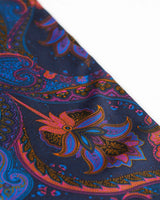 Angled closer view of the navy-blue silk scarf with focus on the ornate purple, orange, pink and black paisley patterns.