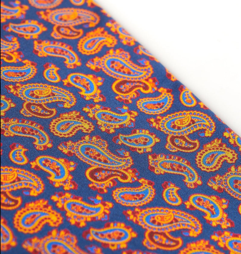 Angled view of the gorgeous deep blue and orange patterned 100 percent silk scarf, presenting a closer view of the small red and gold paisley patterns.