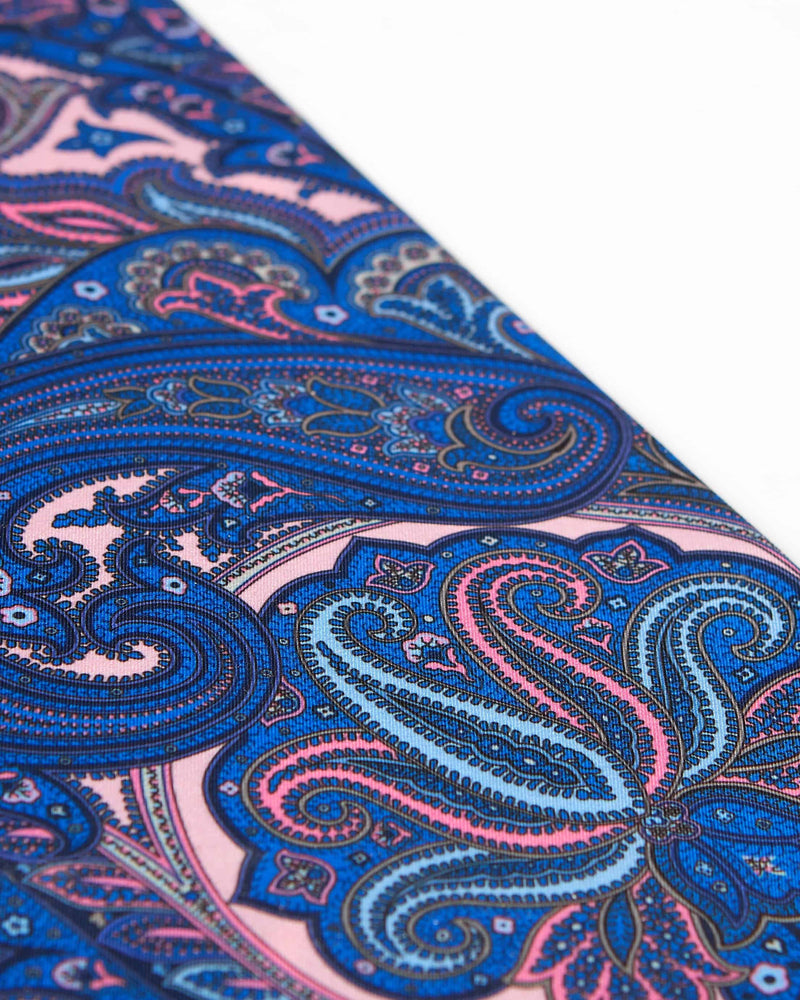 Closer, diagonal angled view of the blue and fuchsia paisley patterns of ‘The Trafalgar’ wool-silk scarf.
