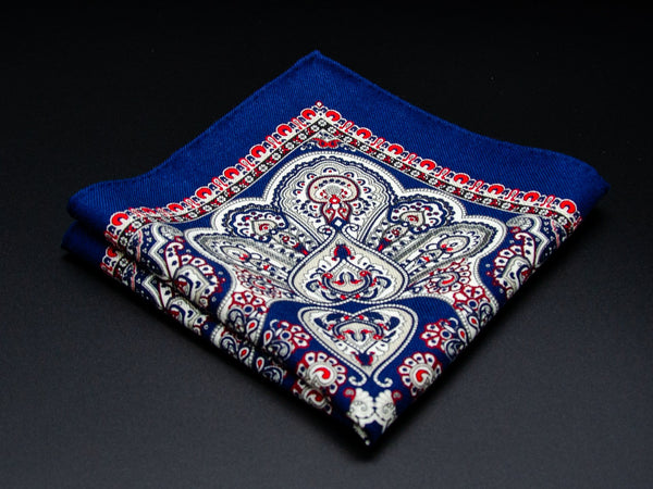 Pure wool 'Pirita' navy pocket square folded into a quarter, clearly showing the heart-shaped paisley motifs and ornate red border.
