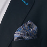 Silk square handkerchief presented in a ‘cone’ and placed in a suit jacket pocket, showing the blue paisley patterns enhanced with white and grey accents.