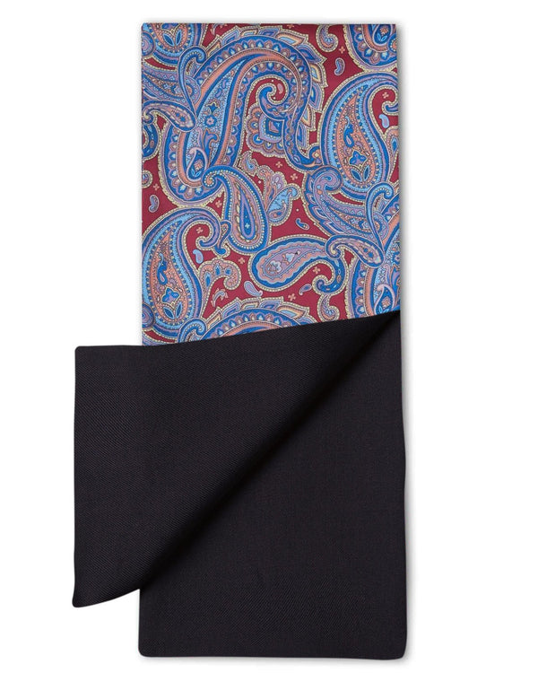 ‘The Hedge' dress scarf arranged in a rectangular shape with deep red fabric and blue paisley patterns. The bottom-right quadrant is folded back to reveal the fine woollen lining underneath the pure silk exterior.