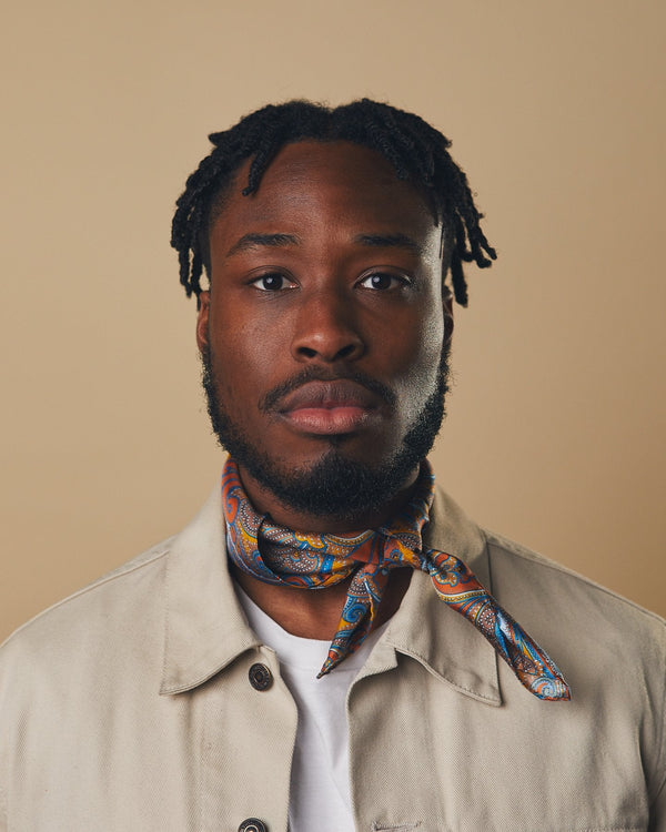 Portrait view of model looking straight ahead, wearing  'The Carnaby' neckerchief tied in a simple knot, showing the intricate paisley patterns.